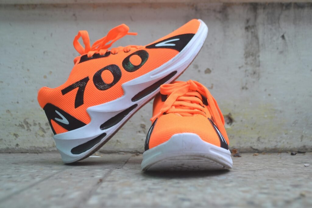 Close-up of bright orange sneakers with number 700 displayed prominently, resting on pavement.