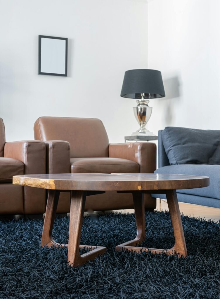 Light living room with wooden table on carpet near leather armchairs and couch near lamp and painting on wall