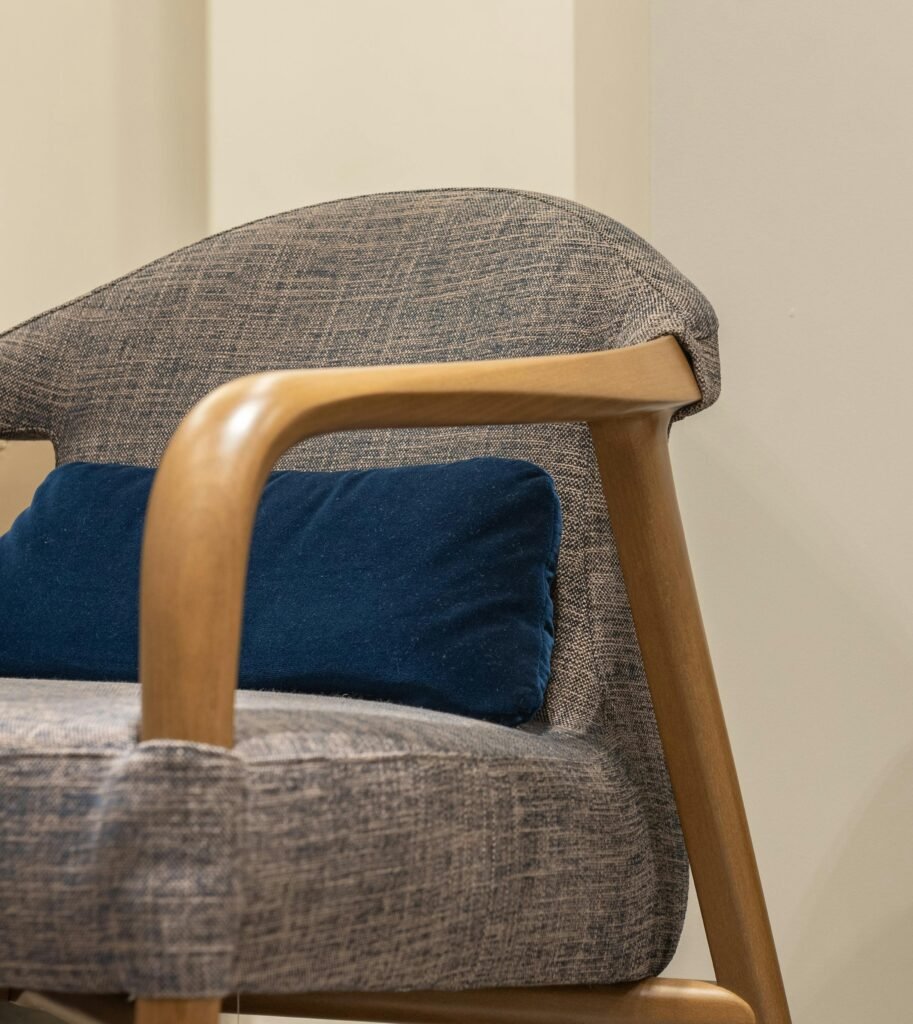 A contemporary gray armchair with wooden armrests and blue cushion, ideal for modern interiors.